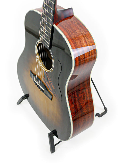 Acoustic guitar on stand against white background with focus on wood detail and strings.