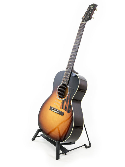 An acoustic guitar with a sunburst finish on a black stand against a white background.
