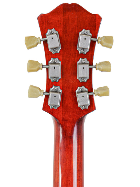 Back of a guitar headstock with six tuning pegs on a red wood grain background.