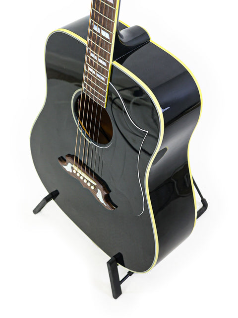 Black acoustic guitar, Gibson Custom Shop Elvis Dove, elegantly positioned on a stand with a white background.