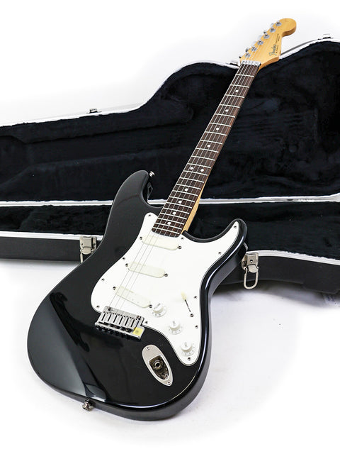 Black electric guitar, Fender Strat Plus USA 1991, displayed in its case on a clean white background.