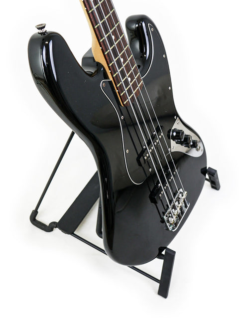Black electric guitar, a 2005 Fender Jazz Bass, positioned on a stand.