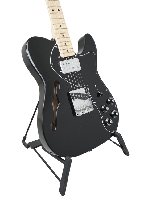 Black electric guitar on a stand with a maple neck and white pickguard.