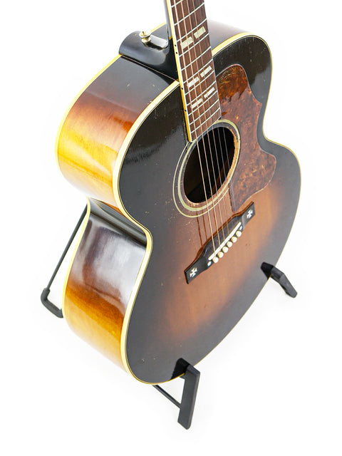 Classic 1952 Gibson J-185 guitar on a stand, featuring a striking white background that emphasizes its vintage appeal.