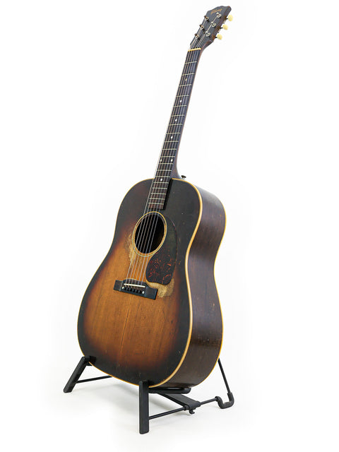 Classic 1953 Gibson J-45 guitar resting on a stand, highlighted by a simple white background.