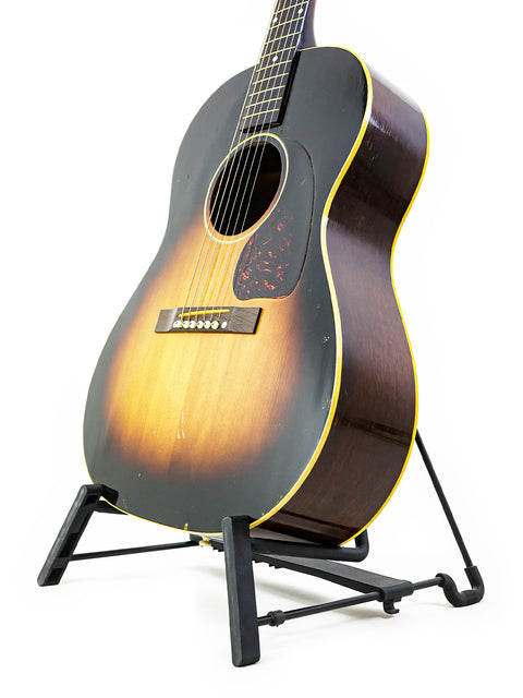 Classic 1954 Vintage Gibson LG-1 guitar resting on a stand, set against a bright white background for emphasis.