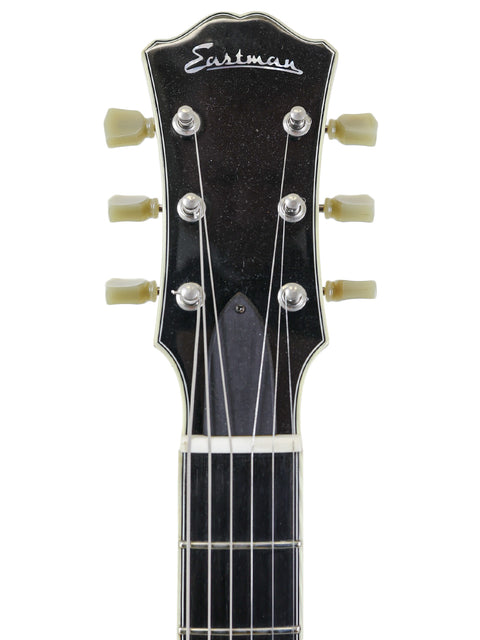 Close-up of a black Eastman guitar headstock with tuning pegs and logo.