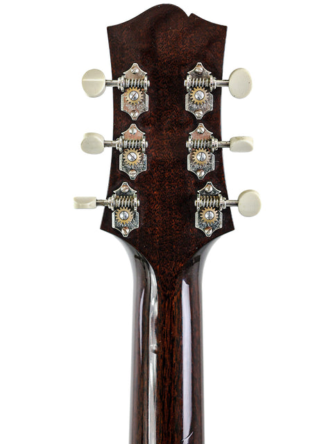 Close-up of a guitar headstock with silver tuning pegs on a dark wood background.