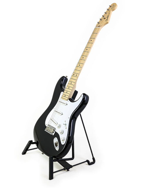 Fender Eric Clapton "Blackie" Stratocaster guitar in black, elegantly positioned on a stand with a white background.
