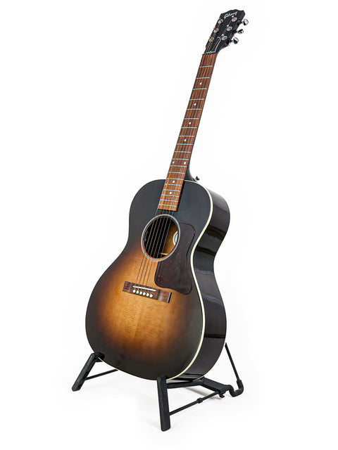 Gibson L-00 Standard Vintage Sunburst guitar displayed on a stand, highlighting its beauty against a bright white backdrop.