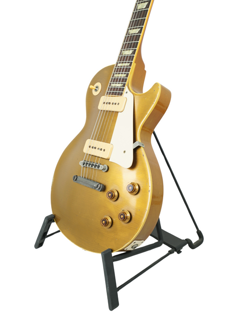 Gold Gibson Les Paul 1956 Reissue guitar displayed on a stand with a white backdrop.