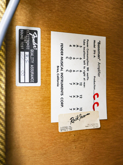 Labels on a wooden surface including a Fender quality assurance tag and a specification label for a Bassman Amplifier.