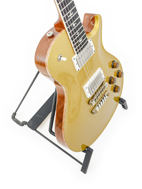 PRS McCarty Singlecut 594 guitar in gold resting on a black stand, highlighting its stunning finish and quality.