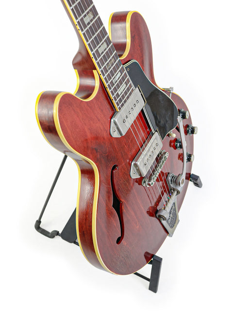 Red 1965 Gibson ES-330 guitar with a black stand, highlighting its vintage charm.