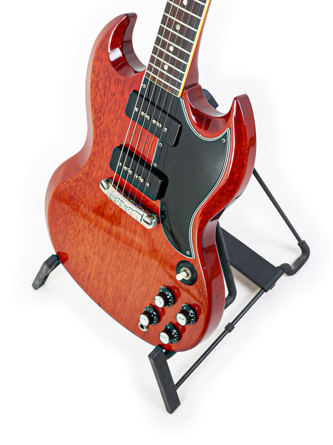 Red Gibson SG Special guitar from 1964/5 on a stand, featuring a black guitar strap for added style.