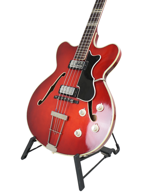 Red Hofner Verithin Bass guitar from 1961, elegantly positioned on a stand with a stark white backdrop.
