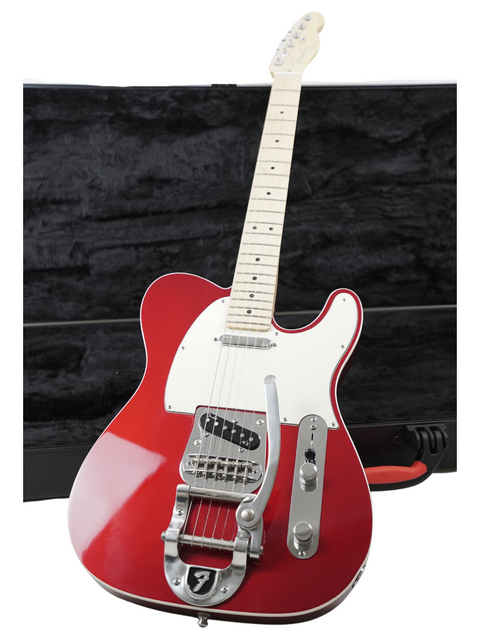 Red electric guitar with a white pickguard leaning against a black amplifier.