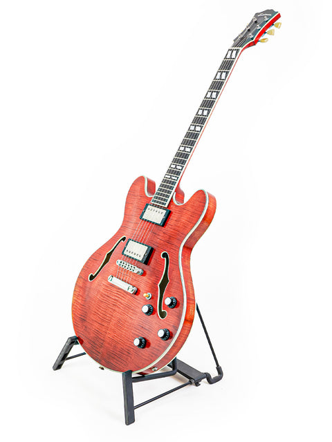 Red semi-hollow electric guitar on a stand against a white background.