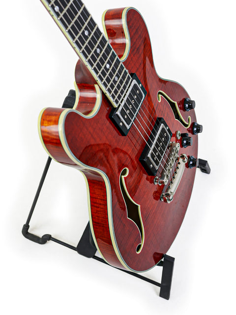 Red semi-hollow electric guitar on stand with white binding on a white background.