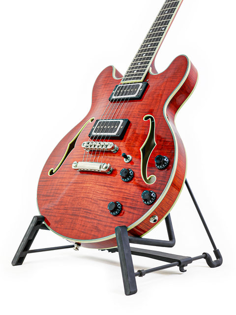 Red semi-hollow electric guitar with f-holes on a stand against a white background.