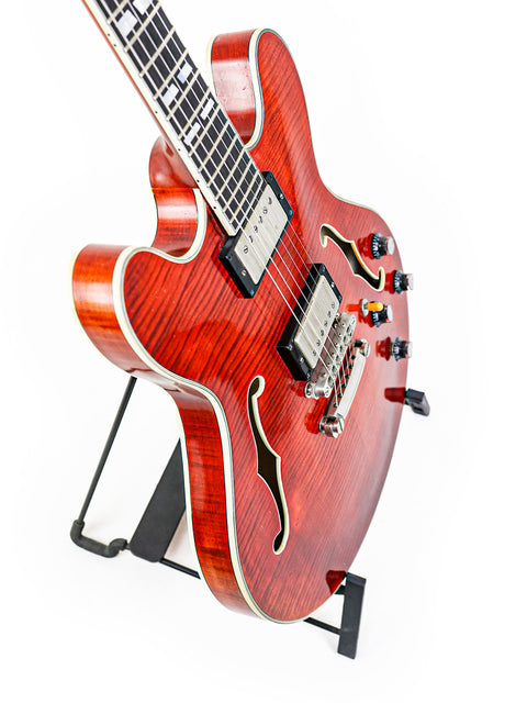 Red semi-hollow electric guitar with f-holes on a stand, white background.