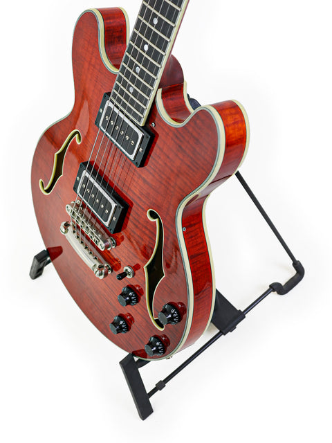 Red semi-hollow electric guitar with f-holes on a stand, white background.