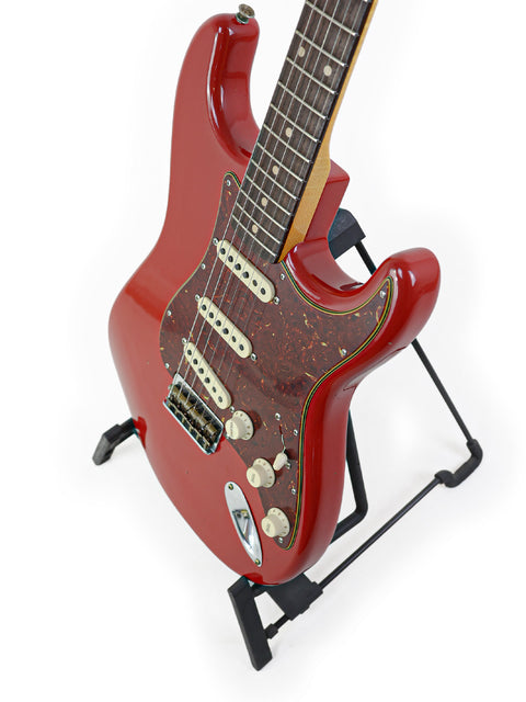 The Fender Custom Shop 1961 Stratocaster Hardtail in Dakota Red rests on a stand, highlighting its classic electric guitar design.