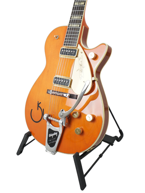 Vibrant orange body of the Gretsch Roundup 6121W Reissue guitar showcased on a stylish black stand, a must-have for players.