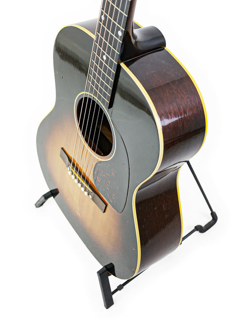 Vintage Gibson LG-1 guitar from 1954 resting on a stand, set against a bright white background for a striking look.