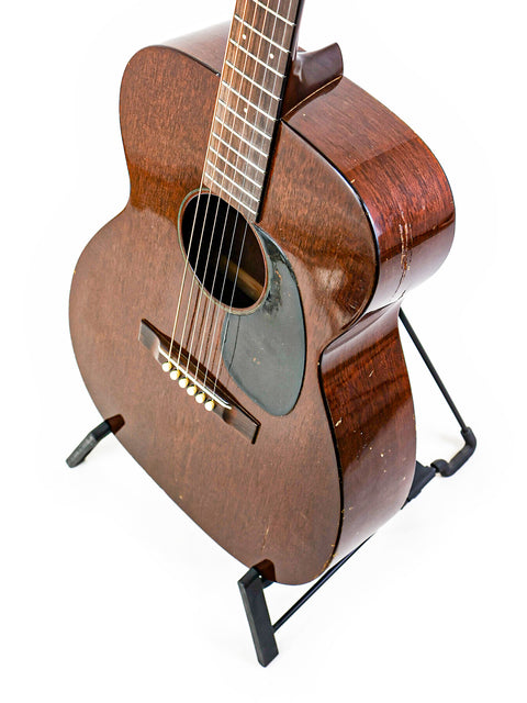 Vintage Martin 00-17 guitar from 1954 positioned on a stand, contrasted against a white background to accentuate its features.