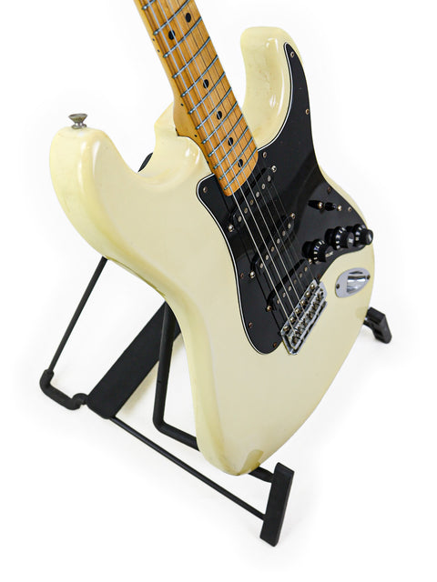 White 1977 Fender Stratocaster electric guitar on a sleek black stand, showcasing its vintage charm.
