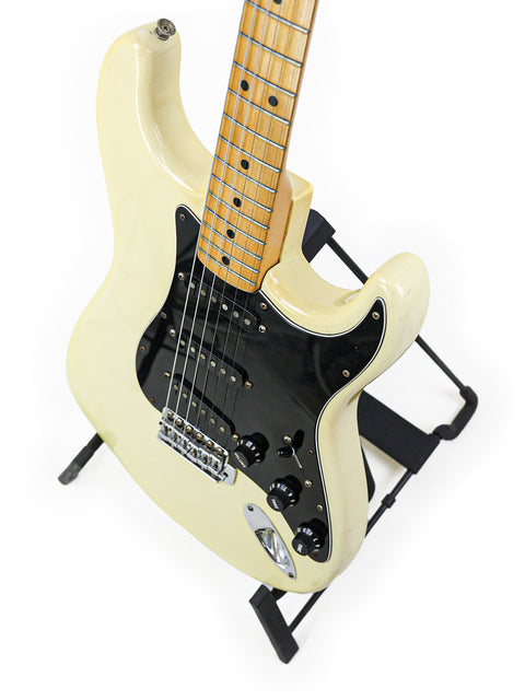 White 1977 Fender Stratocaster electric guitar on a stand, featuring a stylish black pick guard for a classic look.