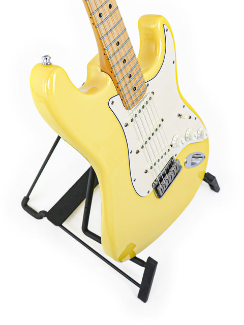Yellow electric guitar on a black stand against a white background.