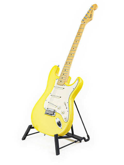 Yellow electric guitar on a black stand against a white background.