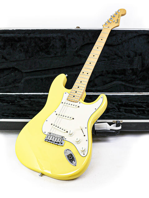 Yellow electric guitar with a maple neck leaning against an open case.