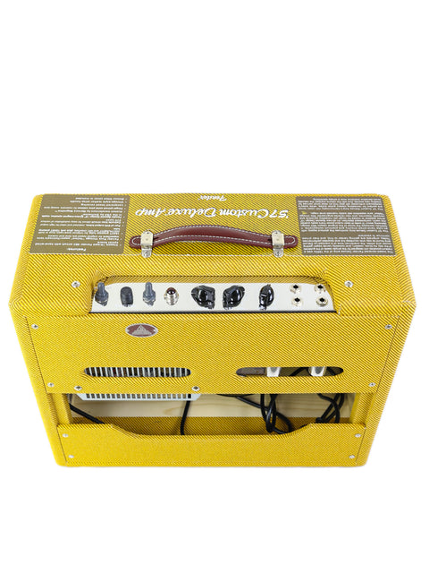 Yellow tweed guitar amplifier with knobs and inputs, lying on its back.