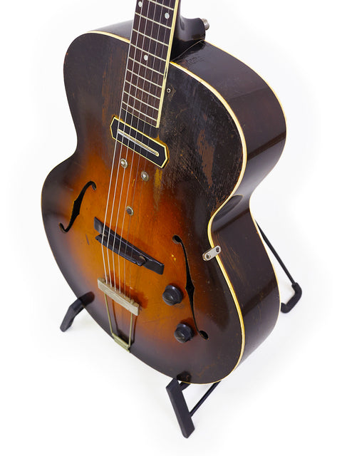  1938 Gibson ES-150 guitar featuring a sunburst finish, elegantly positioned on a stand, highlighting its vintage charm.