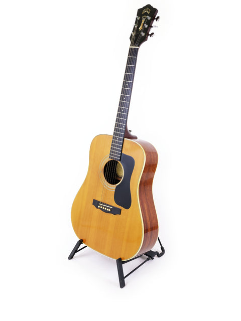 1974 Guild D-50 Bluegrass Special guitar positioned on a stand, set against a bright white background.