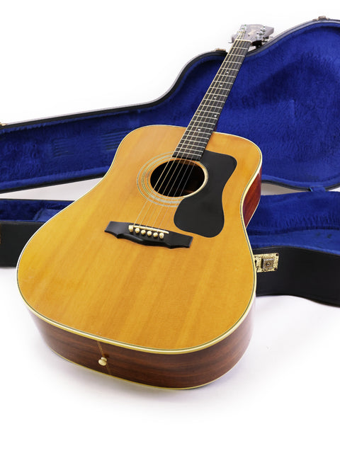 1974 Guild D-50 Bluegrass Special guitar with its case, set against a stark white backdrop.
