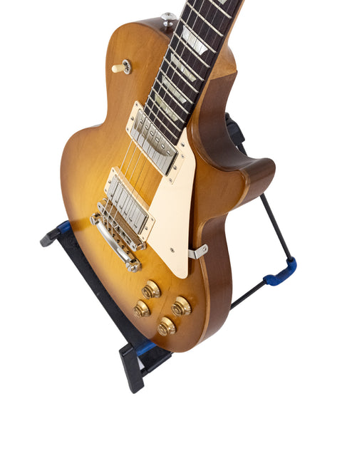  2019 Gibson Les Paul Tribute guitar is positioned on a blue stand, showcasing its stylish design and quality craftsmanship.
