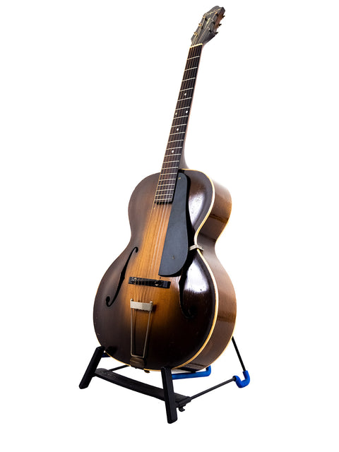 A 1935 Vintage Epiphone Masterbilt Zenith guitar displayed on a stand, set against a pristine white backdrop.
