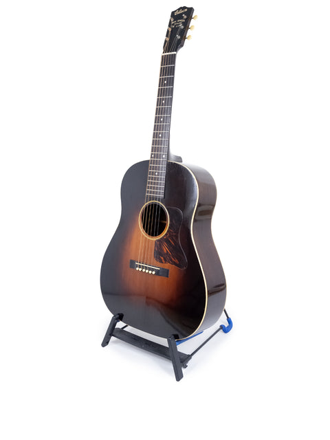 A 1935 Vintage Gibson Roy Smeck Stage De Luxe guitar displayed on a stand with a white backdrop.
