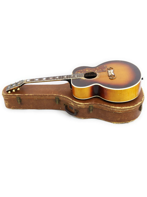 A 1954 vintage Gibson J-200 guitar atop a suitcase, merging musical heritage with travel aesthetics.