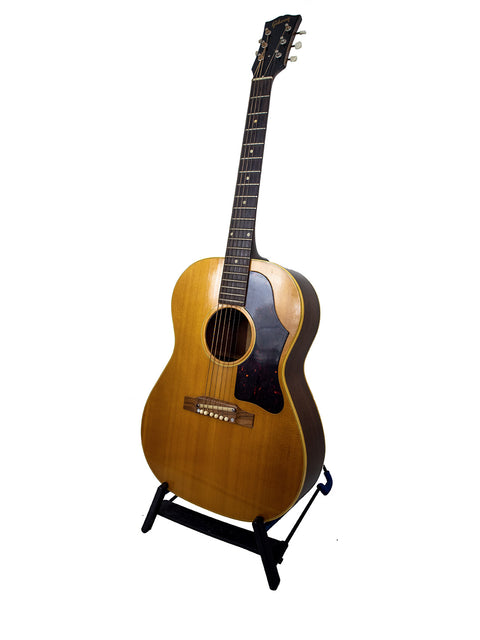 A 1962 Gibson LG-3 Acoustic guitar displayed on a stand with a white backdrop.