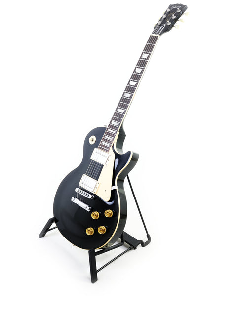 A 1995 Gibson Les Paul Standard guitar in black, elegantly positioned on a stand with a white backdrop.