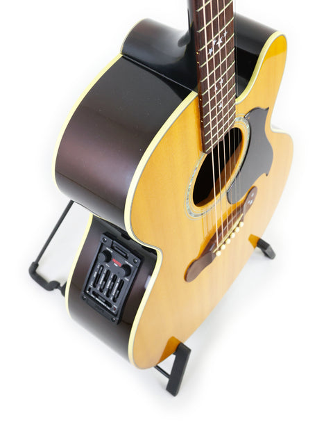 A 2001 Gibson J-180EC guitar is displayed on a stand, with a guitar pick placed next to it.