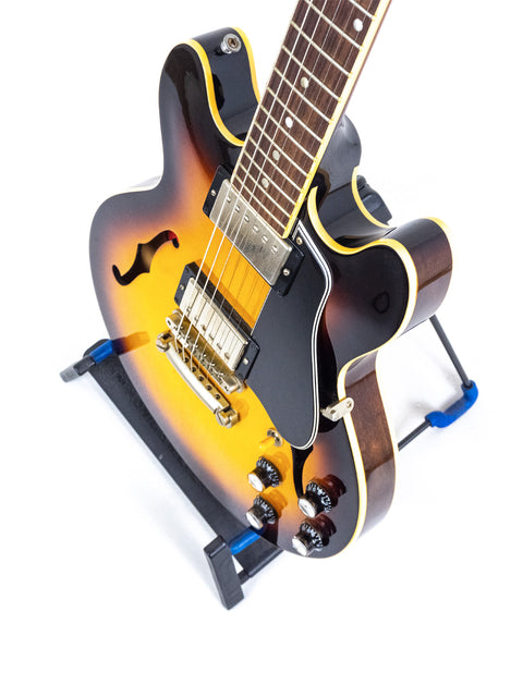 A 2009 Gibson Custom Shop ES 339 guitar rests on a stand, adorned with a stylish blue strap, highlighting its classic appeal.