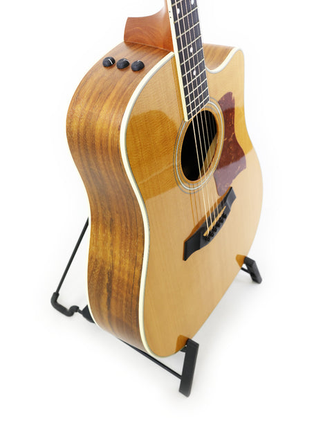 A 2011 Taylor 410CE guitar resting on a stand, featuring a striking white background that emphasizes its beauty.