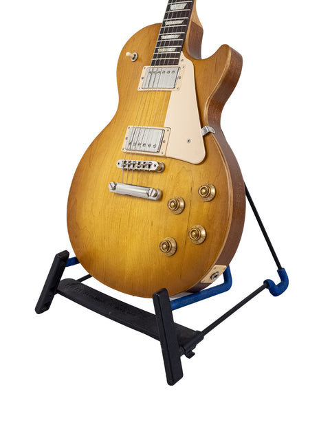 A 2019 Gibson Les Paul Tribute guitar displayed on a blue stand, highlighting its classic shape and vibrant finish.