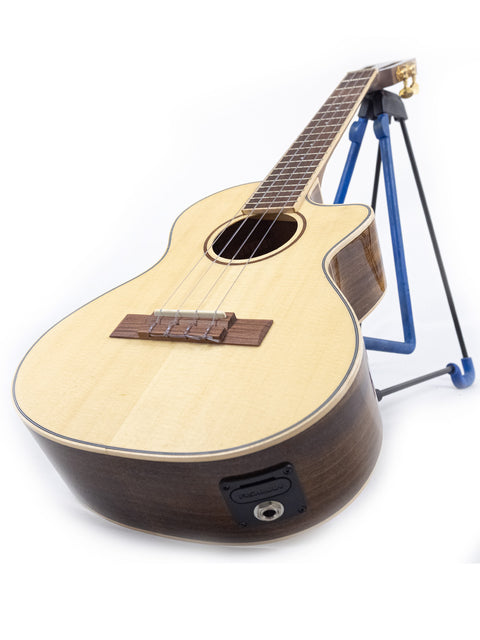 A 2019 Kala KA-SKT GE-C Tenor Ukulele with a pickup, displayed on a blue stand, highlighting its vibrant color and style.